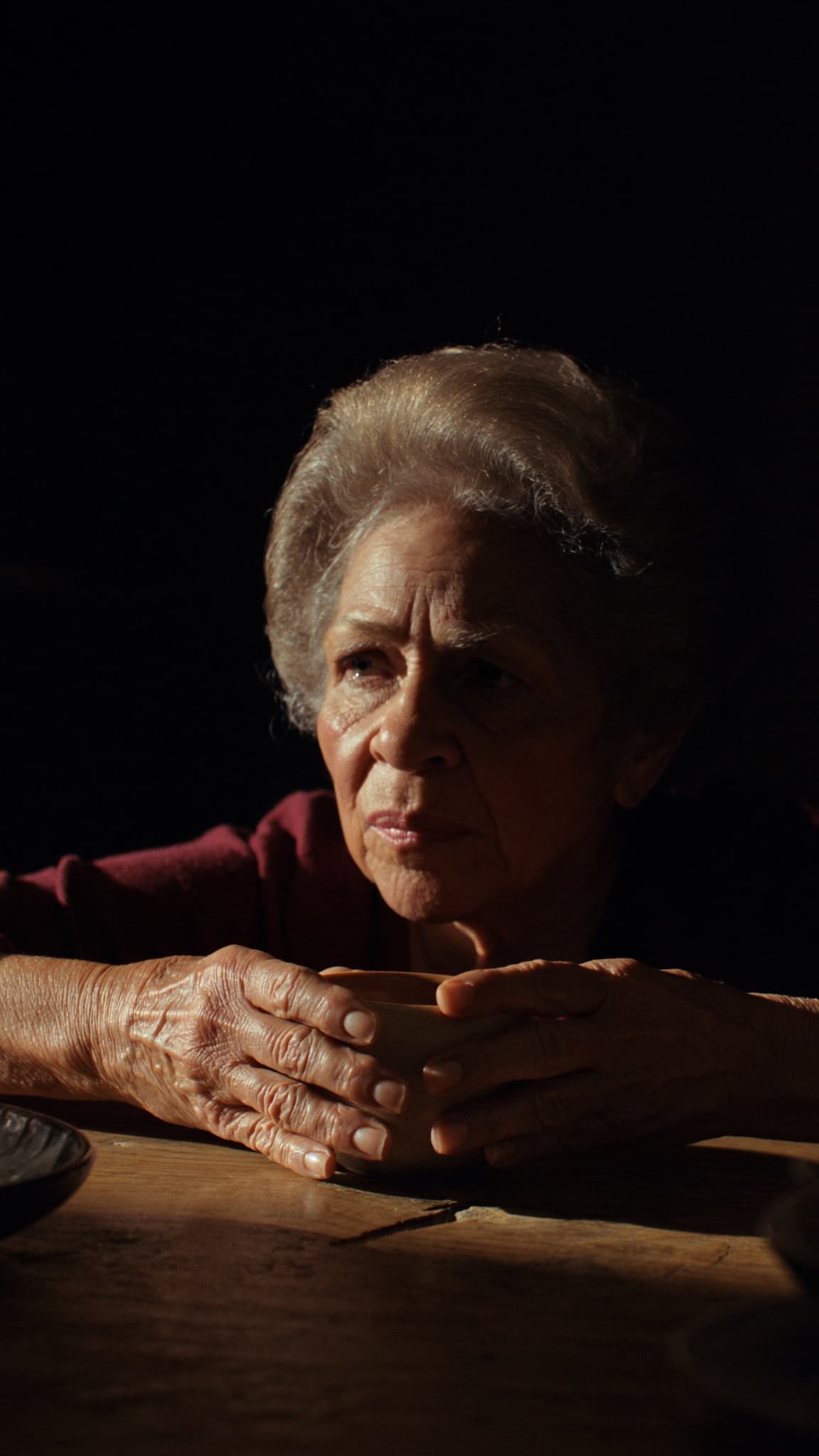 Abuela latina sentada en su cocina sosteniendo café con leche, retrato cinematográfico